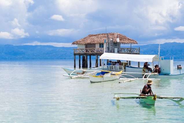 Stilted beach huts on turquoise water with small boats nearby - highlights of Bais Dolphin Watching & Manjuyod Sandbar.